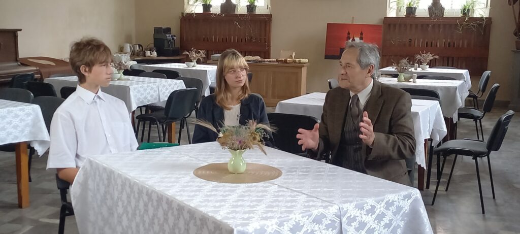 Alicja Waszak i Oliwier Kucharczyk przeprowadzają wywiad z Panem Jerzym Zelnikiem. Wszyscy siedzą przy stole i rozmawiają ze sobą.