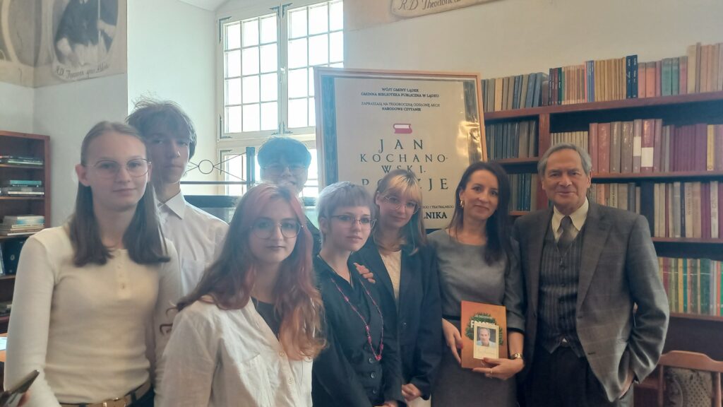 Na zdjęciu, już po oficjalnej części Narodowego Czytania, Pan Jerzy Zelnik stoi razem z Panią Katarzyną Maciochą, opiekunką Koła Dziennikarskiego „Pinezka”, oraz młodzieżą z ZSOiZ. Wszyscy pozują do wspólnego zdjęcia.
