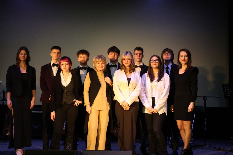 Pani Agnieszka Dzieniakowska oraz Pani Katarzyna Maciocha w towarzystwie uczniów prowadzących uroczystość i młodzieży biorącej udział w przedstawieniu, pozują do zdjęcia na scenie.