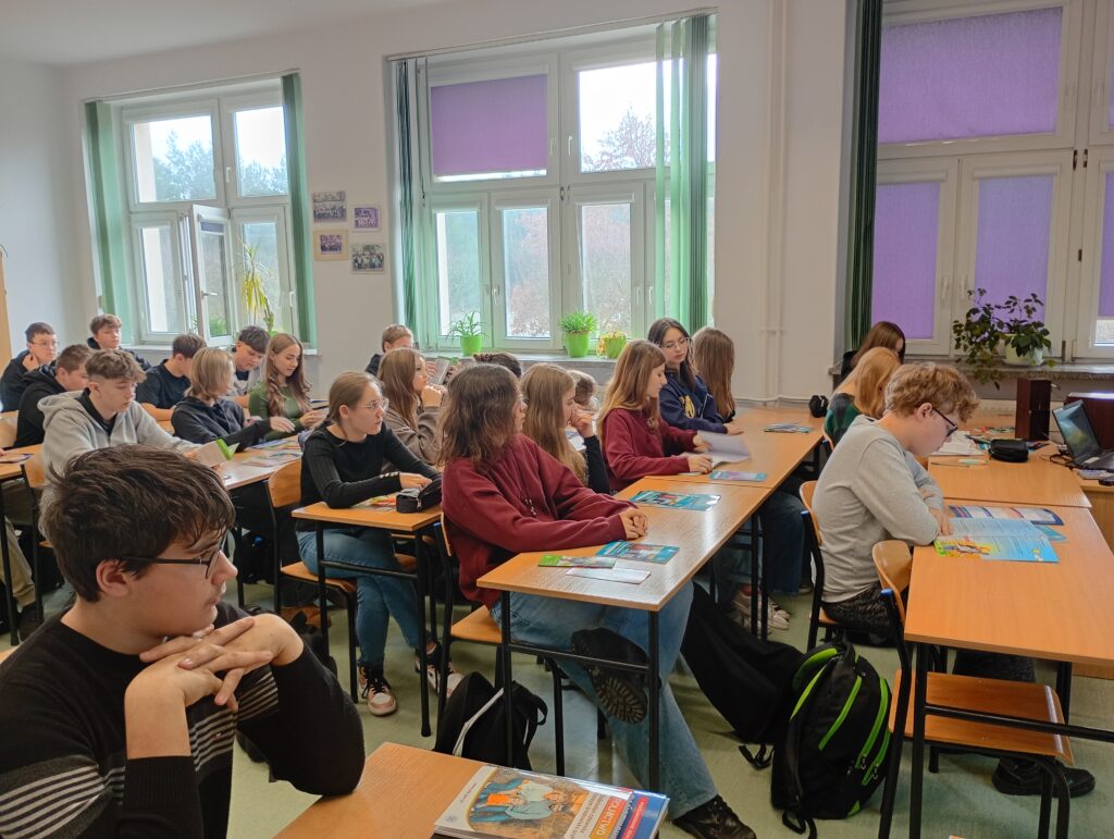 Uczniowie siedzący w ławkach szkolnych czytają materiały dostarczone przez Inspekcję Pracy.