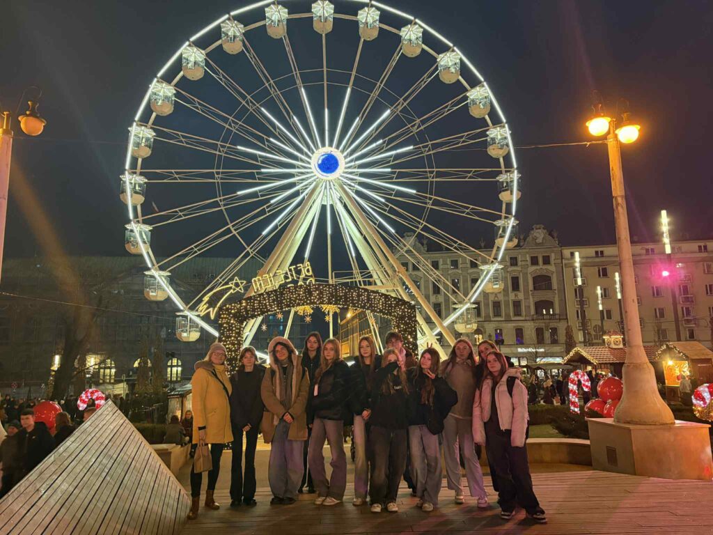 Grupa osób stojąca przed jarmarkiem bożonarodzeniowym