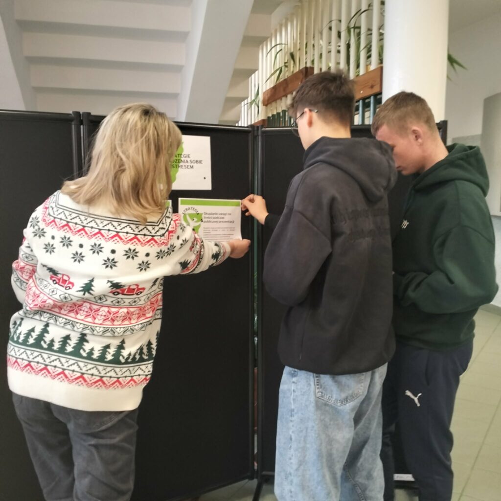 Trzy osoby przygotowują tablicę informacyjną na temat strategii radzenia sobie ze stresem.