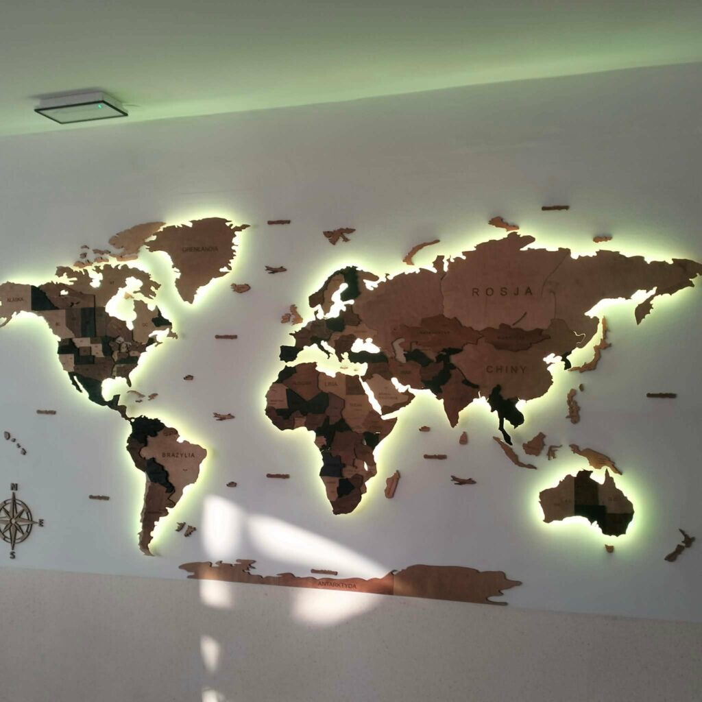 Trójwymiarowa mapa świata z drewnianymi konturami kontynentów i państw, podświetlona od tyłu na ścianie.