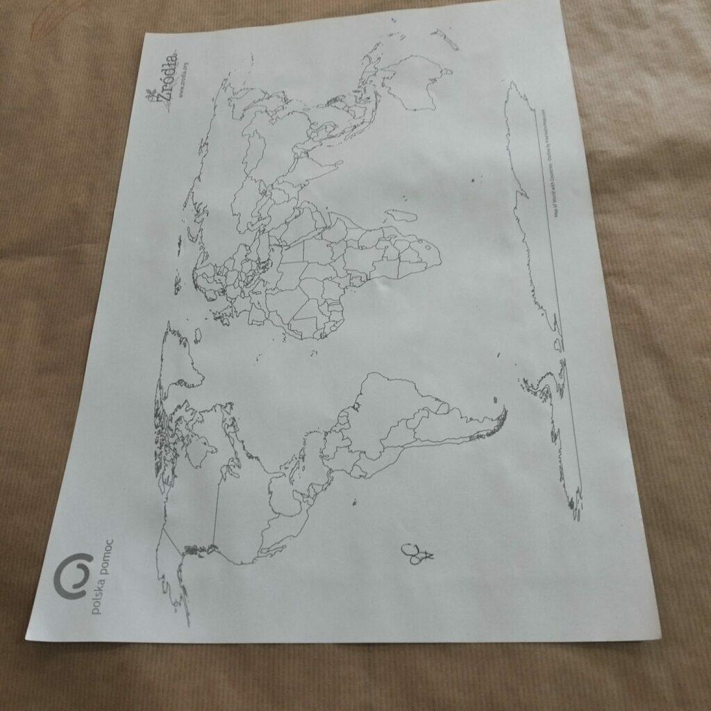 Mapa polityczna świata bez kolorów z wyraźnie zaznaczonymi granicami państw, leżąca na brązowym obiciu.