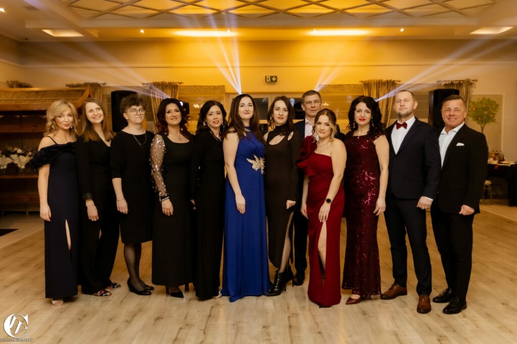 Grupa elegancko ubranych osób pozująca razem na jasnej sali balowej.