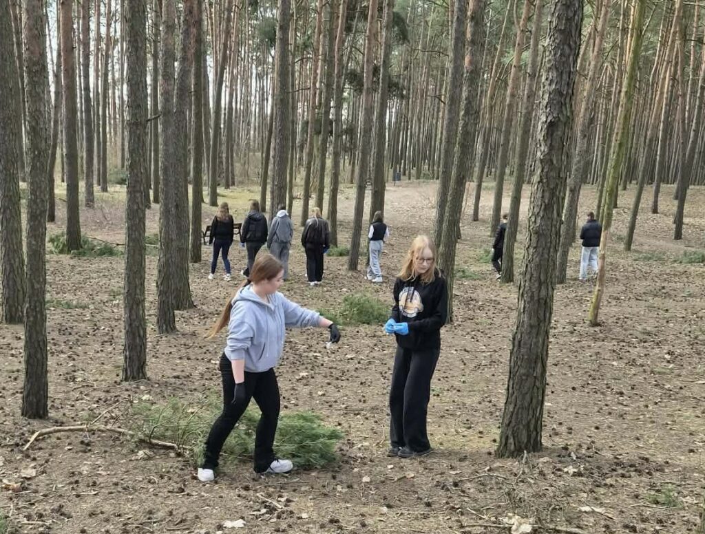 Grupa młodych osób sprzątająca las, zbierająca śmieci i porządkująca teren.