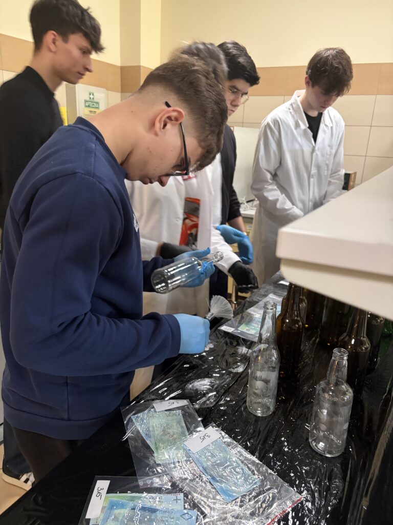 Młodzi ludzie w laboratorium dokładnie czyścić butelki przy stole z zabezpieczonymi dowodami i banknotami.