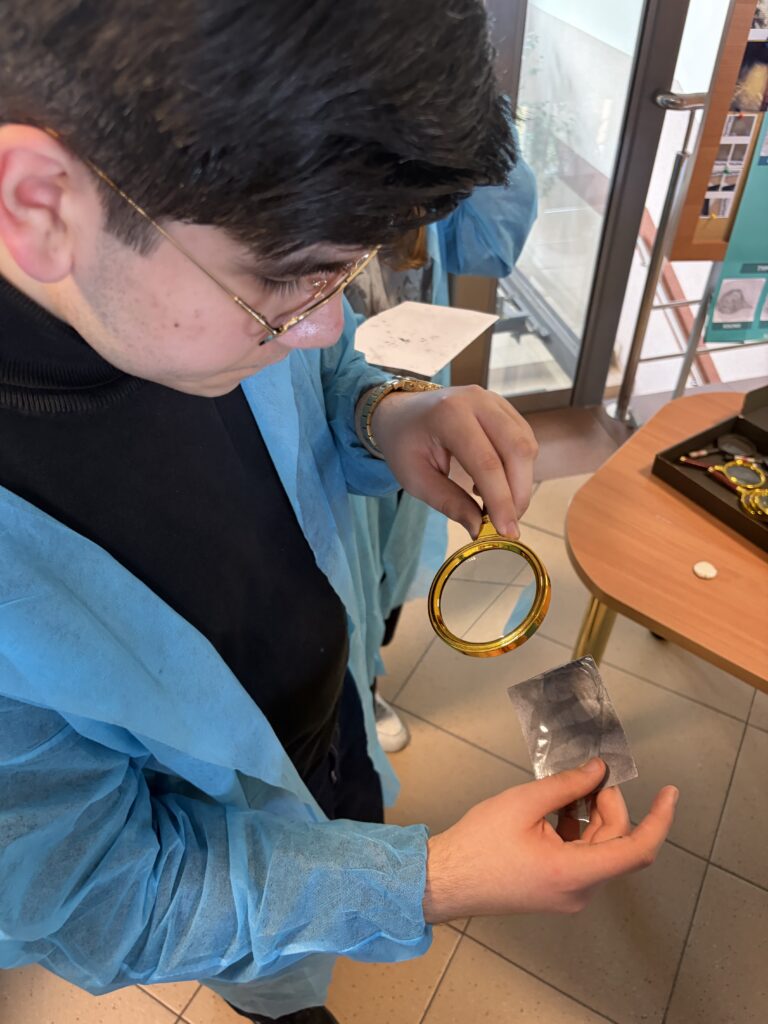 Mężczyzna w niebieskim kitlu ogląda odcisk linii papilarnych za pomocą lupy.