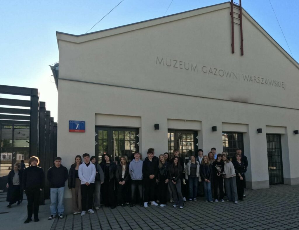 Grupa młodych ludzi stoi przed budynkiem Muzeum Gazowni Warszawskiej przy ulicy ks. Ignacego Kłopotowskiego 7.