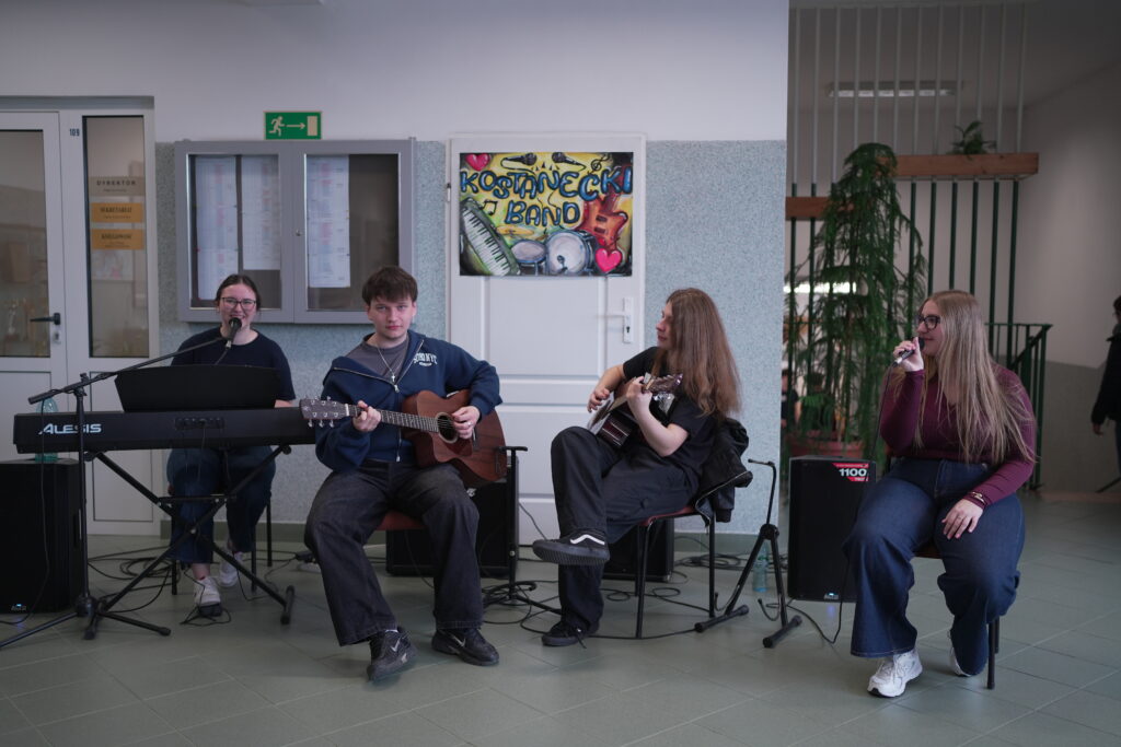 Grupa młodzieży i dwoje dorosłych na tle plakatu z napisem „ZSOiZ Zagórów szkoła z sercem”.