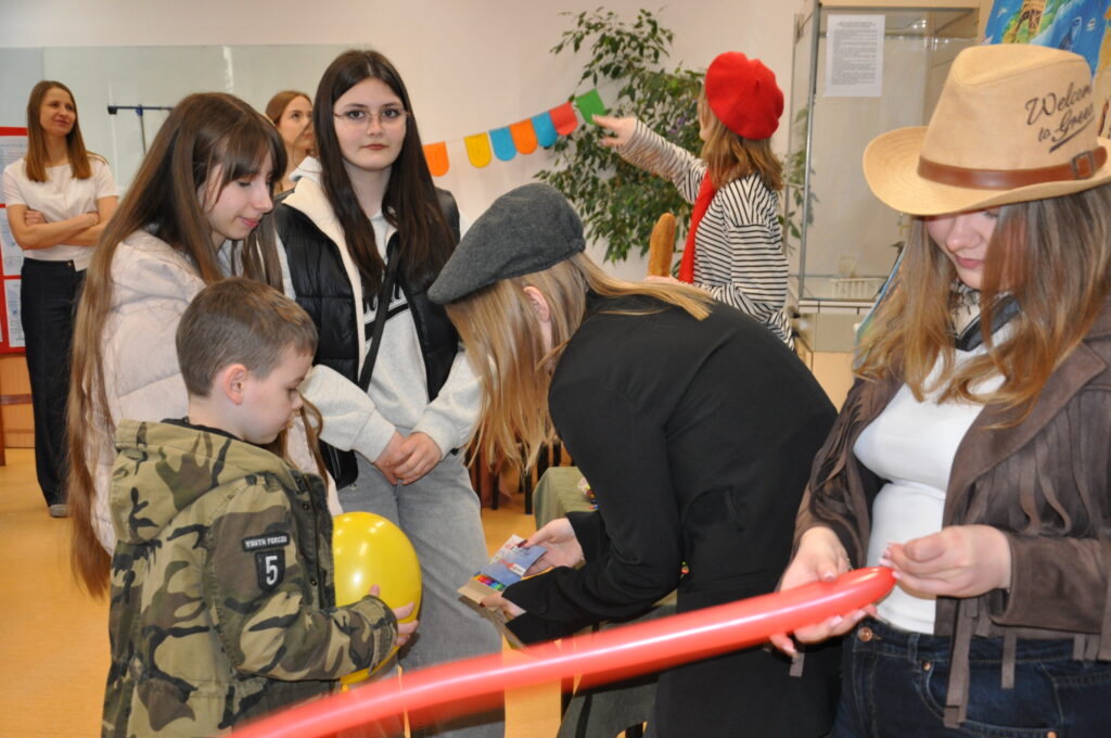 Grupa młodych osób uczestniczy w wydarzeniu, gdzie część z nich trzyma kolorowe balony i materiały promocyjne.