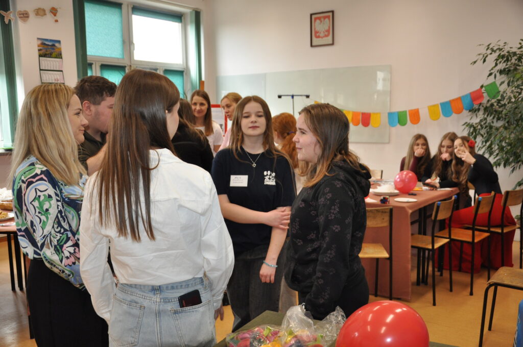 Grupa młodych osób rozmawiających i integrujących się w szkolnej klasie z ozdobami i balonami.
