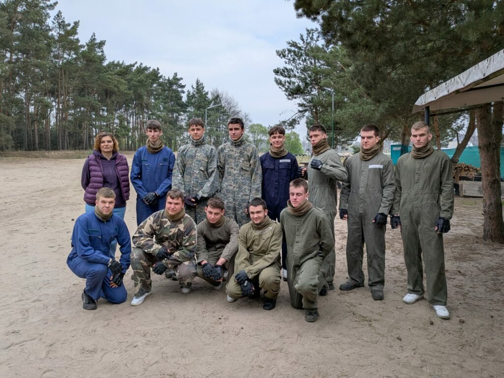 Grupa młodych osób w mundurach i kombinezonach wojskowych pozująca na tle leśnego terenu.
