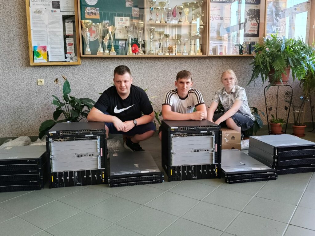 Grupa uczniów pozuje do zdjęcia na tle sprzętu sieciowego