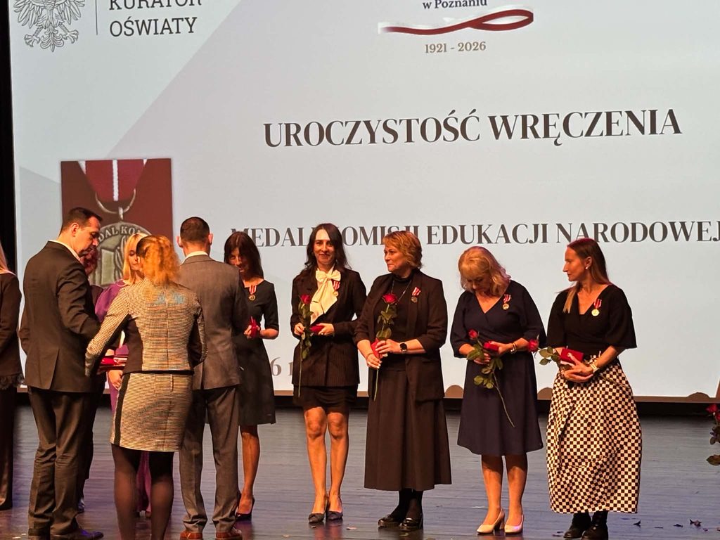 Grupa osób odbiera medale Komisji Edukacji Narodowej podczas uroczystości wręczenia na scenie.