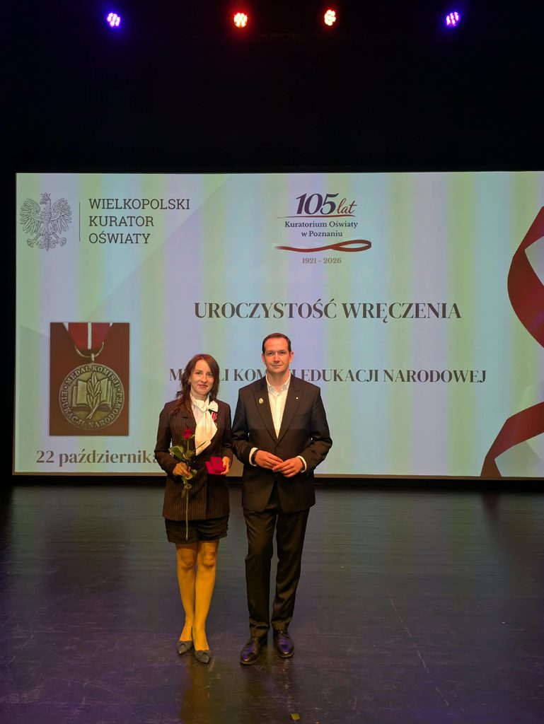 Dwóch elegancko ubranych ludzi stoi na scenie podczas uroczystości wręczenia Medali Komisji Edukacji Narodowej organizowanej przez Wielkopolskiego Kuratora Oświaty.