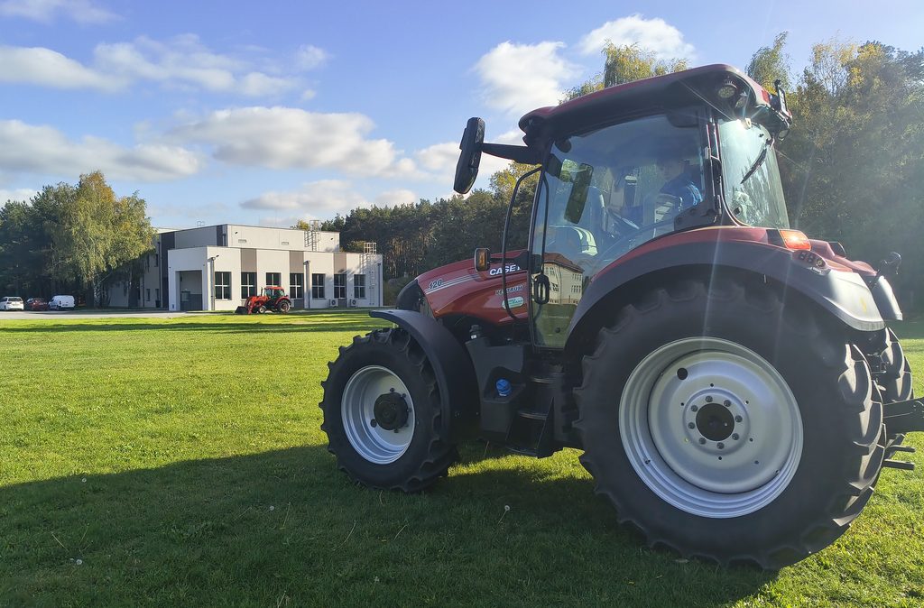 Młody mężczyzna siedzi za kierownicą czerwonego traktora Case IH Vestrum 120 na podwórzu z kostki brukowej.