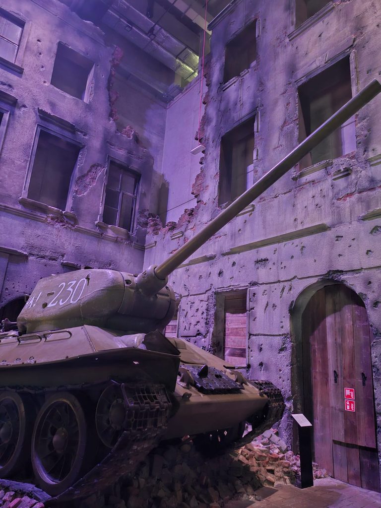 Zniszczony czołg na tle ściany z ruinami budynku, zlicowanej z liczbą „IA-230” na wieży.